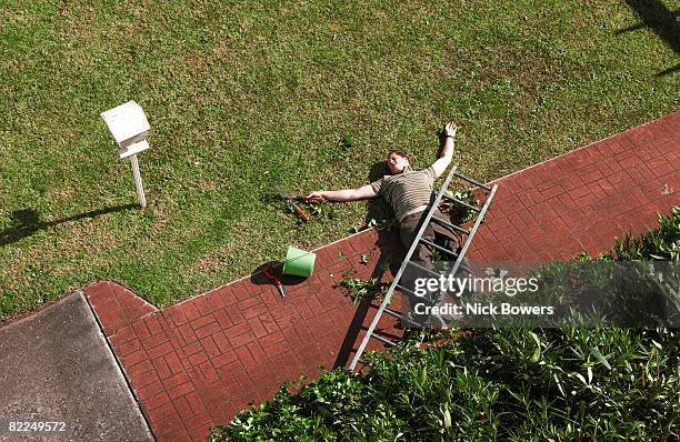man lying on ground with ladder on top of him - bewusteloos stockfoto's en -beelden