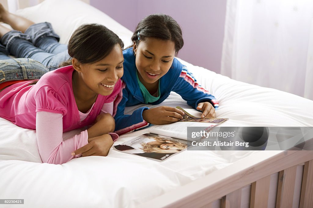 Teenage girls looking at magazine together on bed