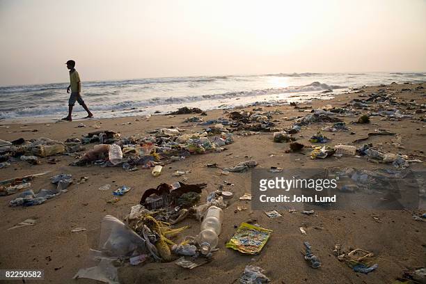 man walking on a beach full of garbage - 海 汚染 ストックフォトと画像