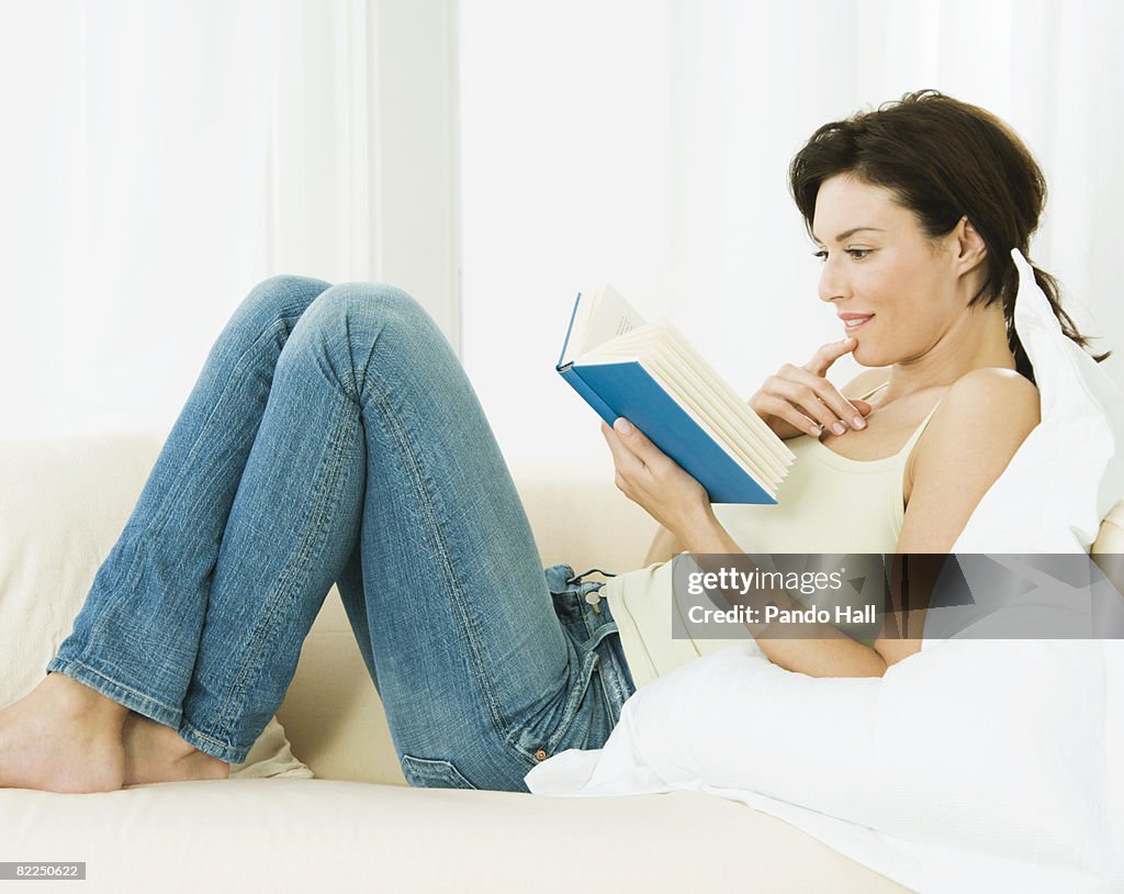 Woman reading book on sofa, side view