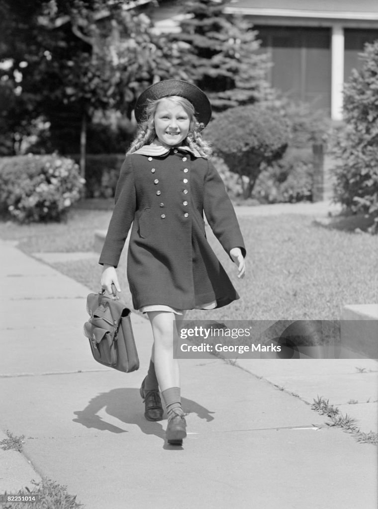 Young girl (8-9) with schoolbag on sidewalk, portrait