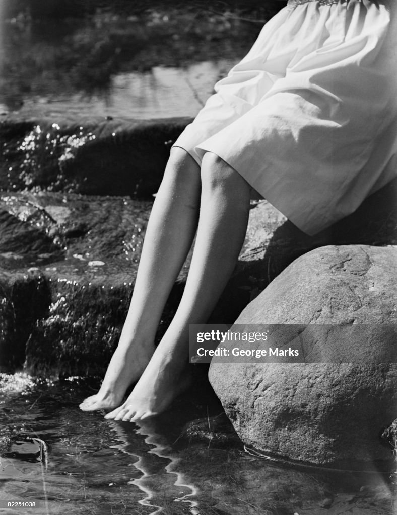 Mulher sentada na rocha com os pés na água, a seção