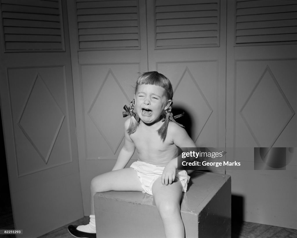 Girl (6-7) sitting on box and crying