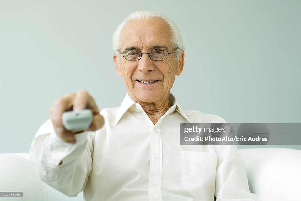 Senior man pointing remote control at camera, smiling