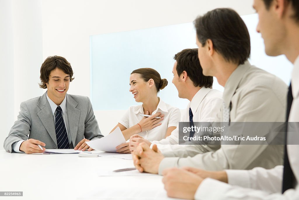 Group of business associates sitting together at conference table, woman smiling at man