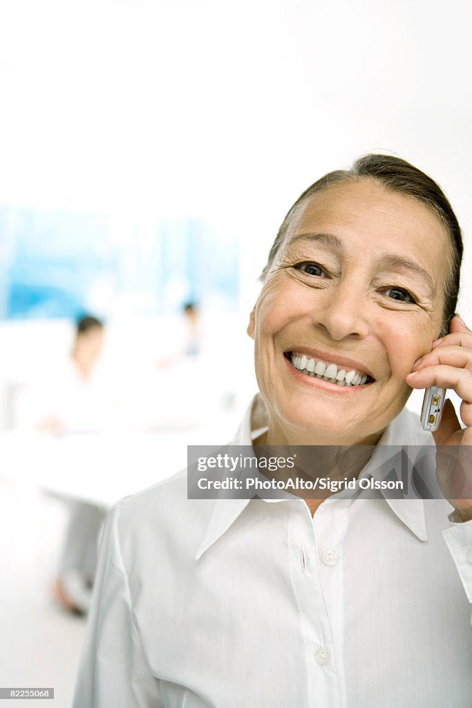 Senior woman using cell phone, smiling at camera