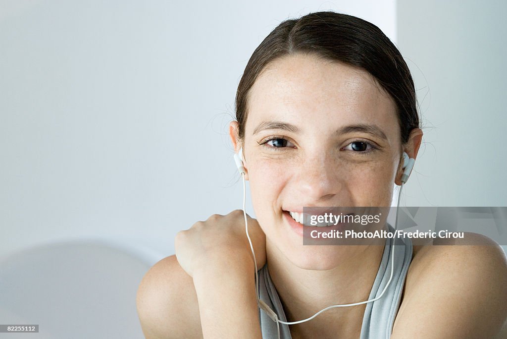 Young woman listening to earphones, smiling at camera