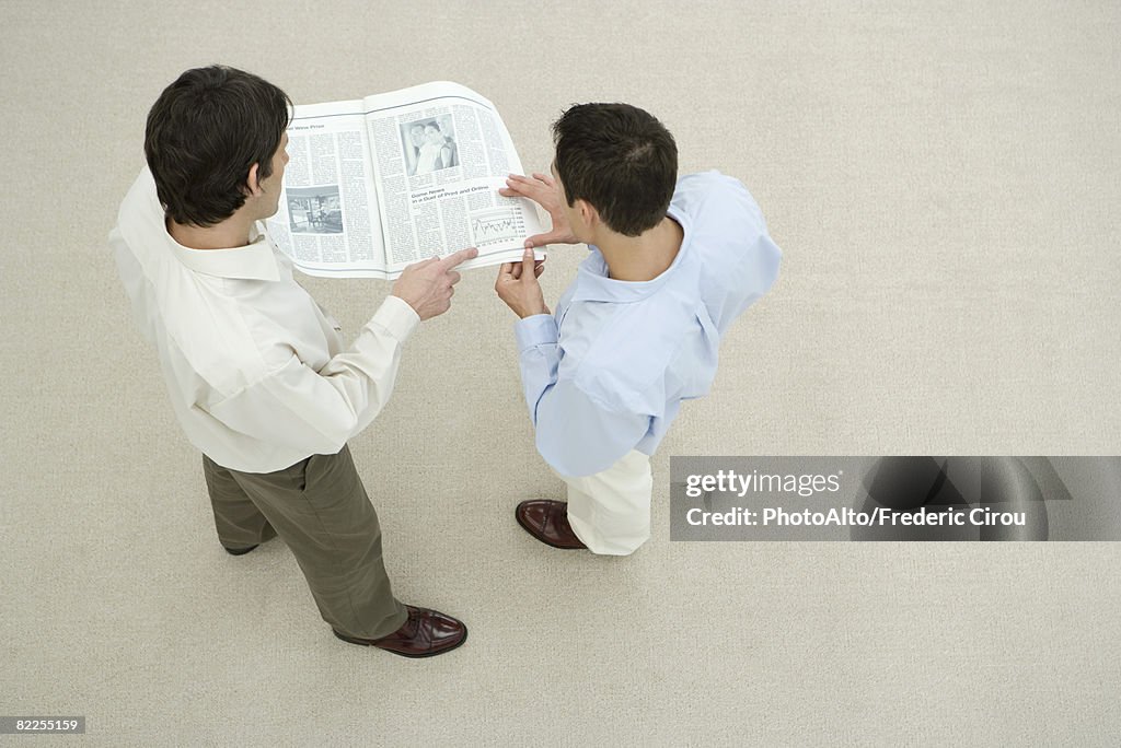 Two men looking at newspaper together, overhead view