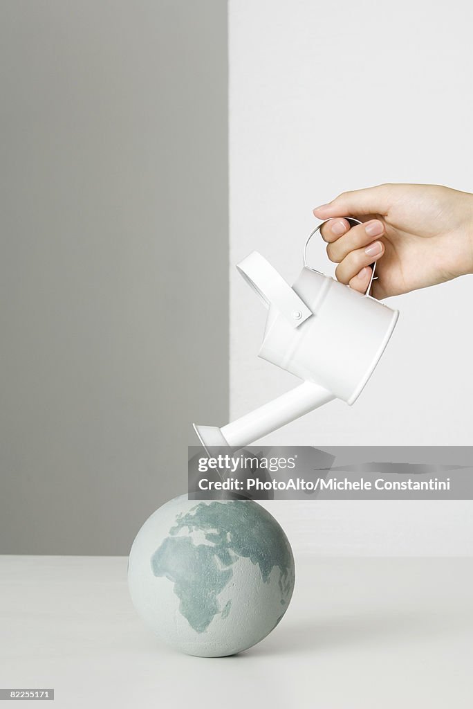 Hand holding watering can over globe