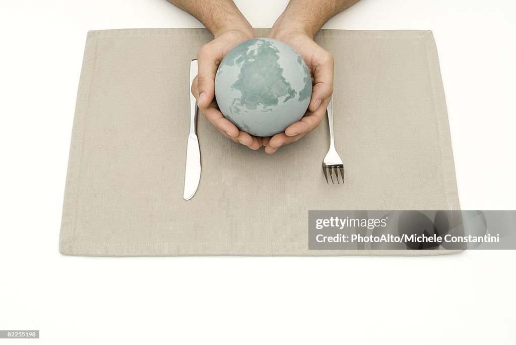 Hands holding globe over placemat and silverware