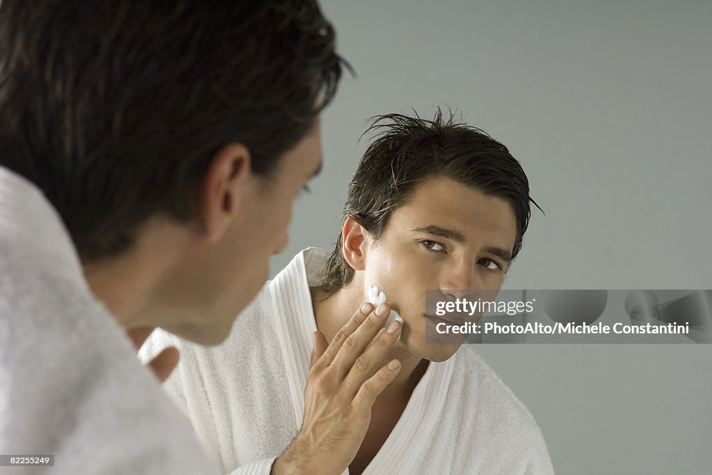 Man looking at himself in mirror, applying shaving cream