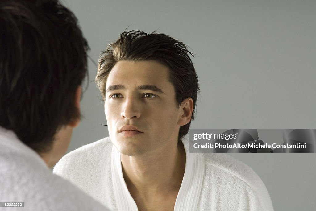 Man examining his face in the mirror, wearing bathrobe