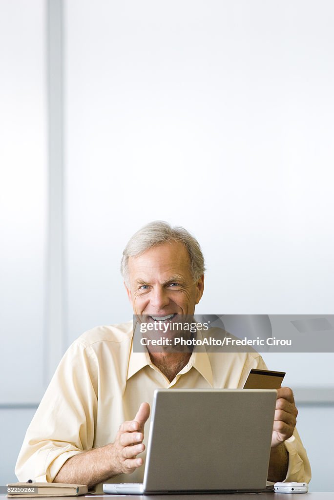 Man making on-line purchase with credit card, smiling at camera