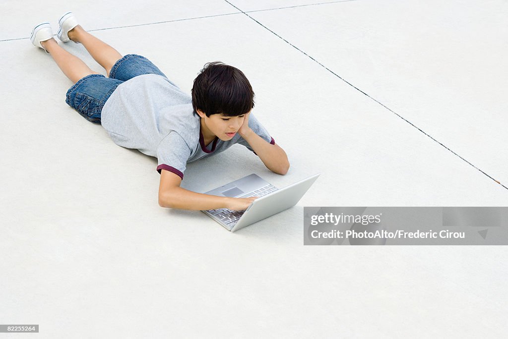 Boy lying on stomach on the ground, using laptop computer