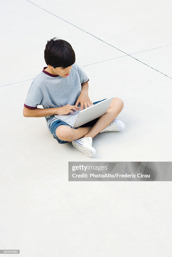 Boy sitting cross-legged on the ground, using laptop