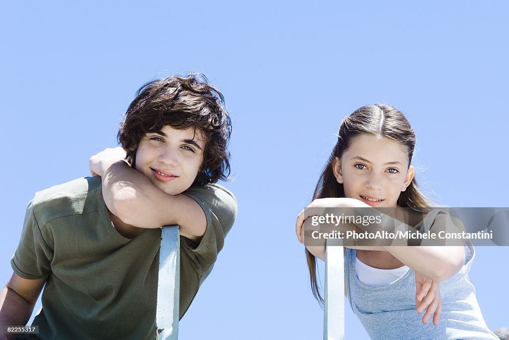 Brother and sister sitting sideways in chairs, leaning on elbows, smiling at camera