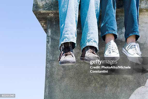 two pairs of legs dangling over concrete ledge - two pair stock pictures, royalty-free photos & images