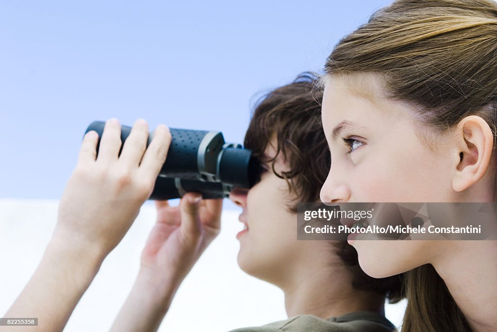 Teenage boy looking away through binoculars, sister nearby, profile