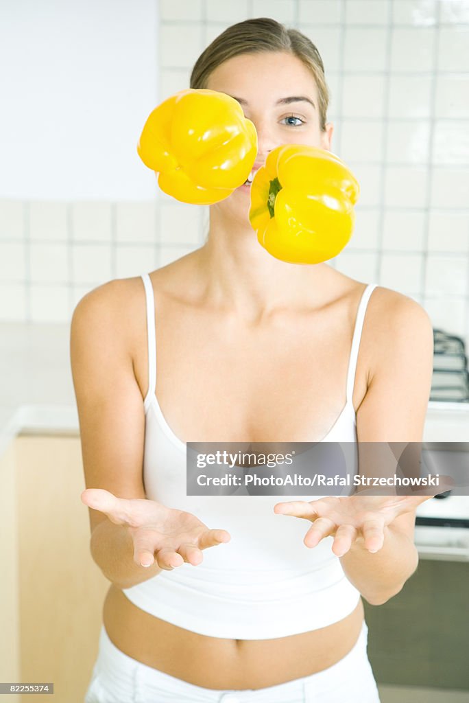 Woman juggling yellow bell peppers in kitchen