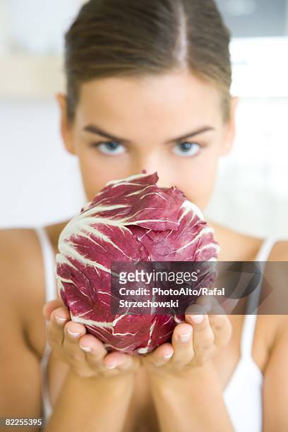 woman holding a head of radicchio lettuce, partially obscuring her face, looking at camera - radicchio stock pictures, royalty-free photos & images