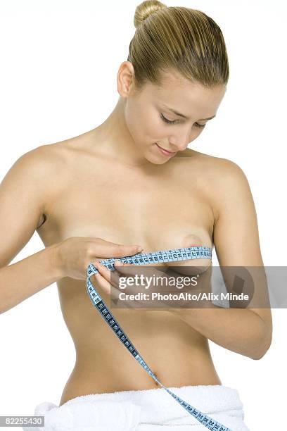 woman wrapping measuring tape around chest, looking down at breasts, smiling - aumento dos seios imagens e fotografias de stock