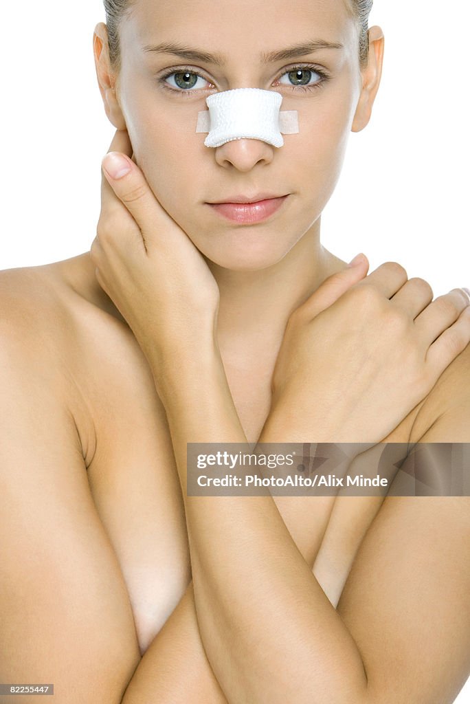 Woman with bandaged nose, arms folded across chest, looking at camera