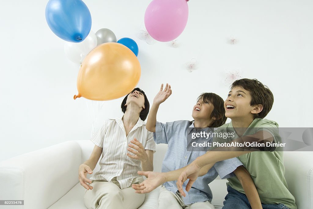 Mother and two sons playing with balloons, looking up