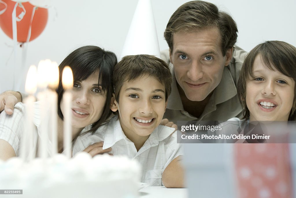 Family in front of birthday cake with lit candles, smiling at camera