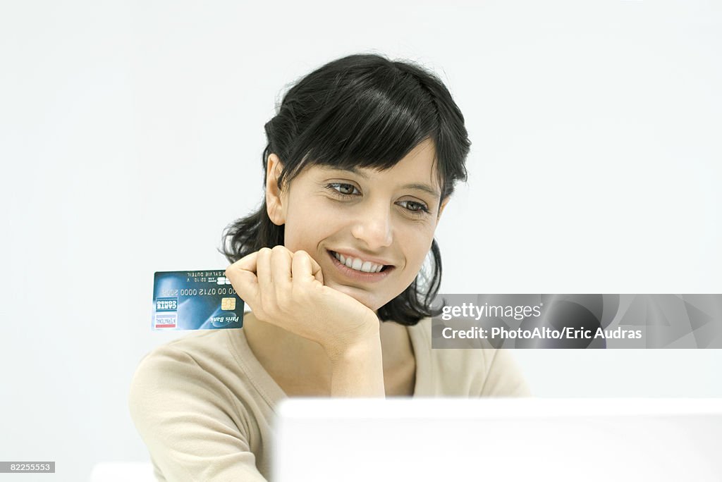 Woman holding credit card, looking at laptop computer, smiling