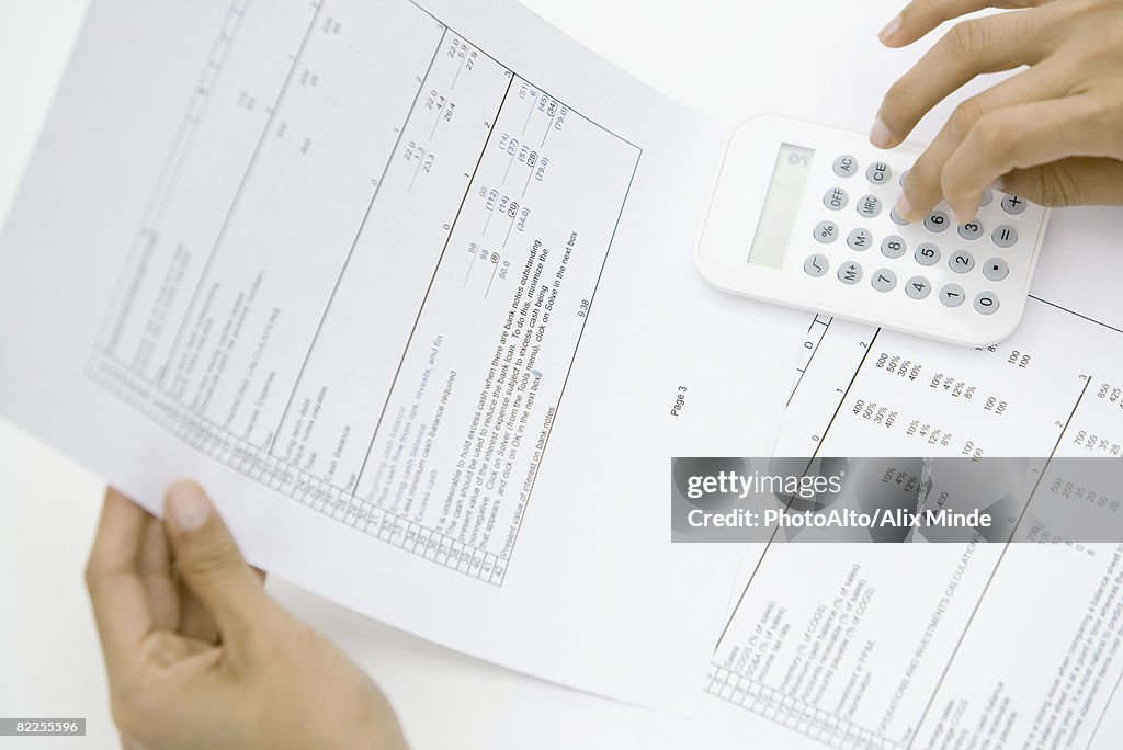 Person holding document, using calculator, cropped view of hands