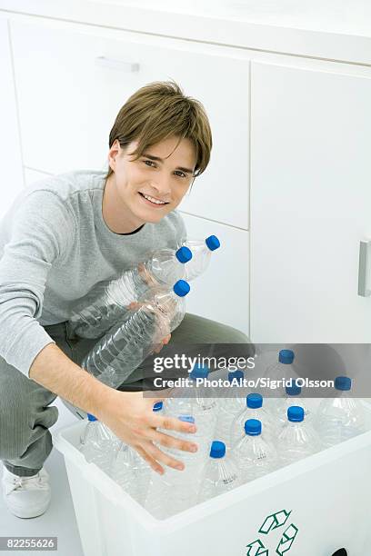 young man putting plastic bottles in recycling bin, smiling at camera - full responsibility stock pictures, royalty-free photos & images