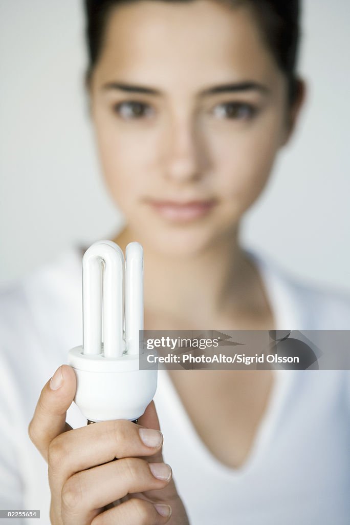 Young woman holding energy efficient light bulb, focus on foreground