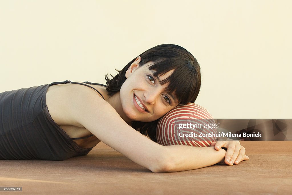 Woman lying on the ground, resting head on ball, smiling at camera