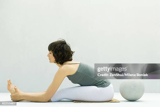 woman stretching on the ground, ball behind her, side view - zehenspitzen berühren stock-fotos und bilder