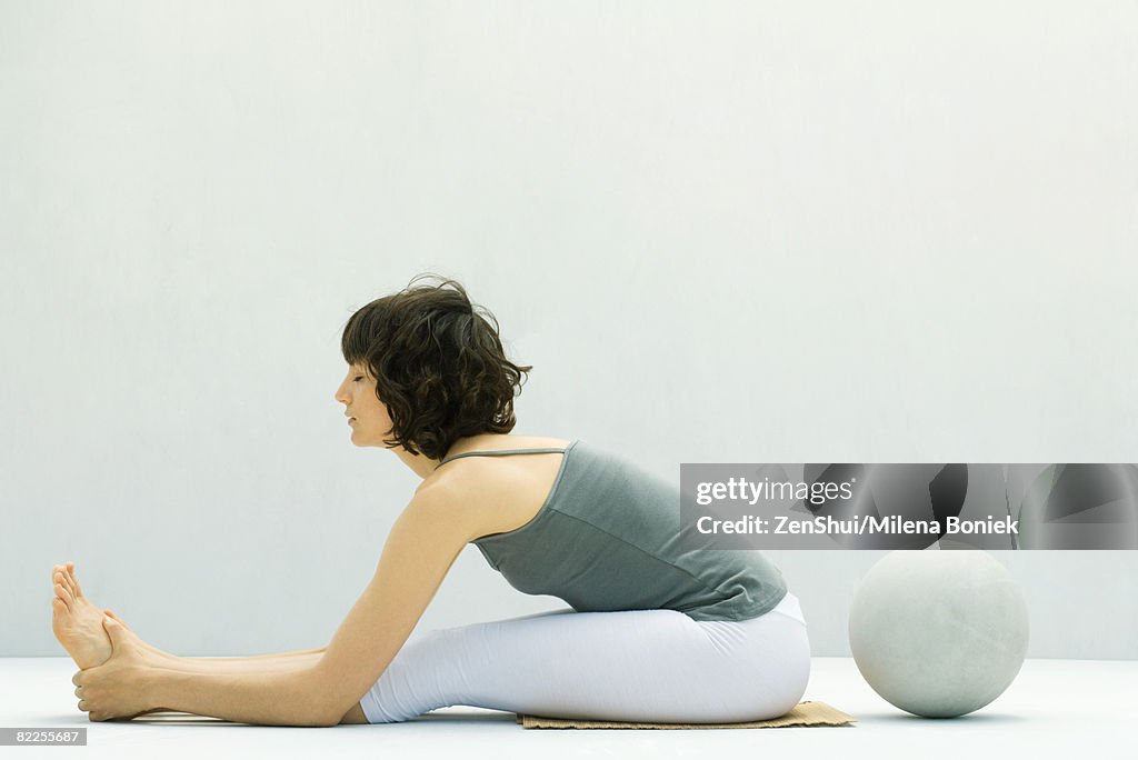 Woman stretching on the ground, ball behind her, side view