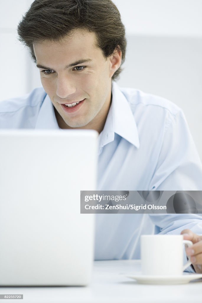 Man using laptop, holding coffee cup