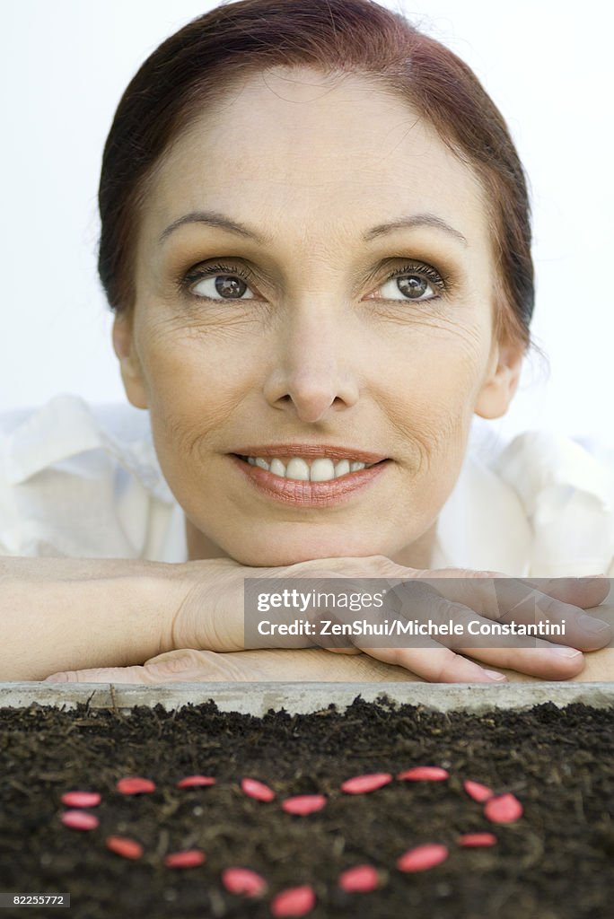 Mature woman with heart shape made of seeds on soil