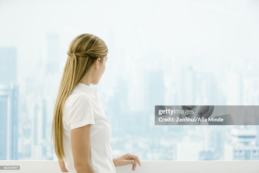 Young woman standing in front window, looking out