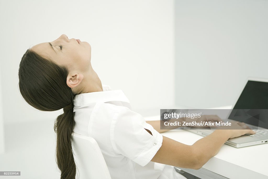 Woman sitting in front of laptop, head back, eyes closed
