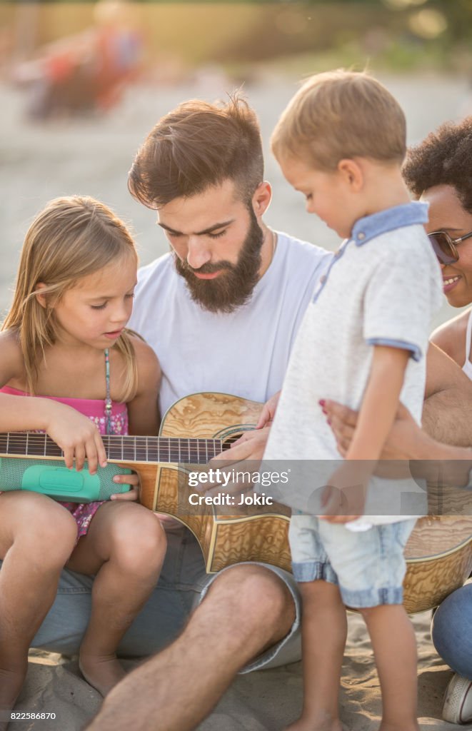 Father explains to children how to play a guitar.