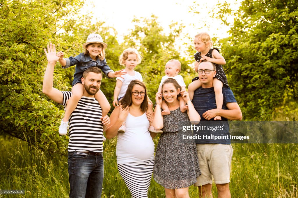 Two young families with childrens, carrying them on shoulders in sunny summer nature.