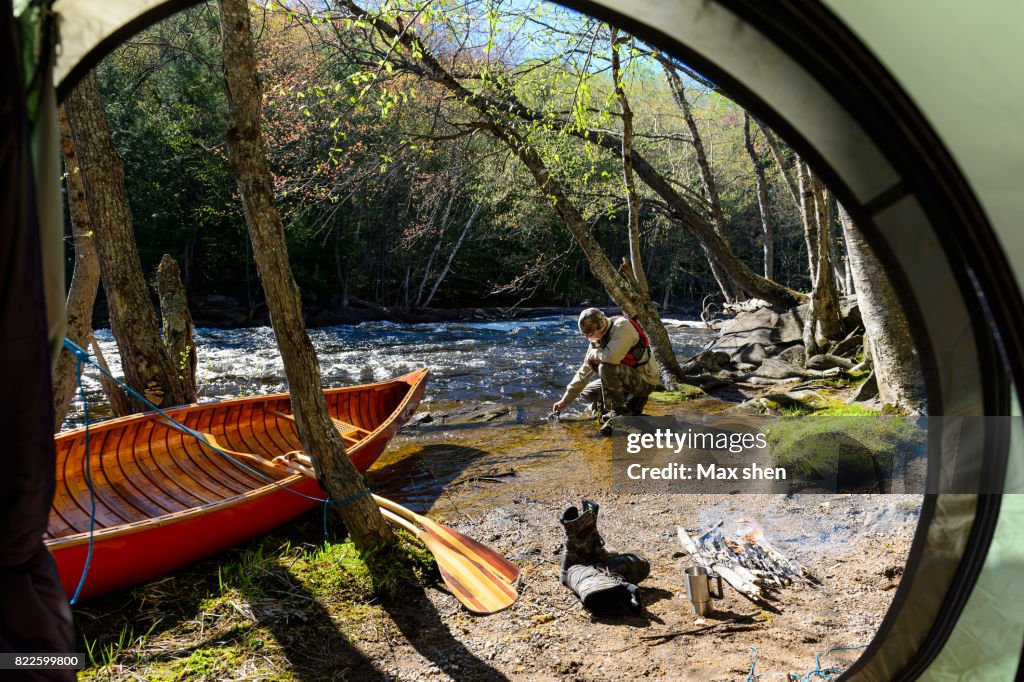 Man camping at the riverbank with a canoe