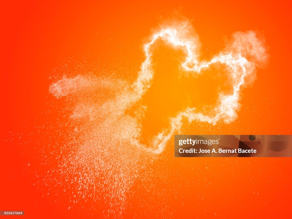 Forms and textures of an explosion of a powder of color white on a  orange background