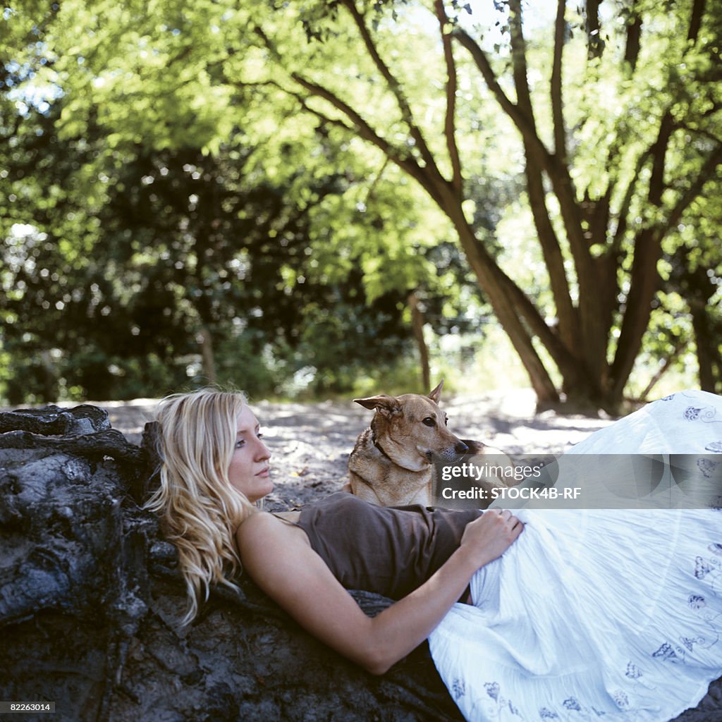 Reflective young woman leaning against trunk, dog beside of her