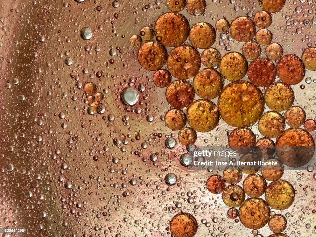 Full frame of the textures formed by bubbles and drops of oil in the form of circle floated on water on a bronze colored background