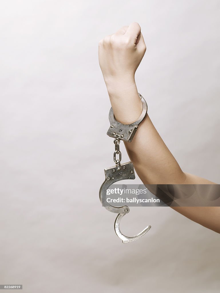 Young asian woman's arm, handcuffs making a fist