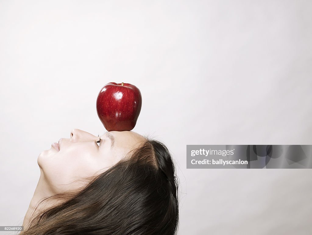 Young asian woman balancing red apple on forehead