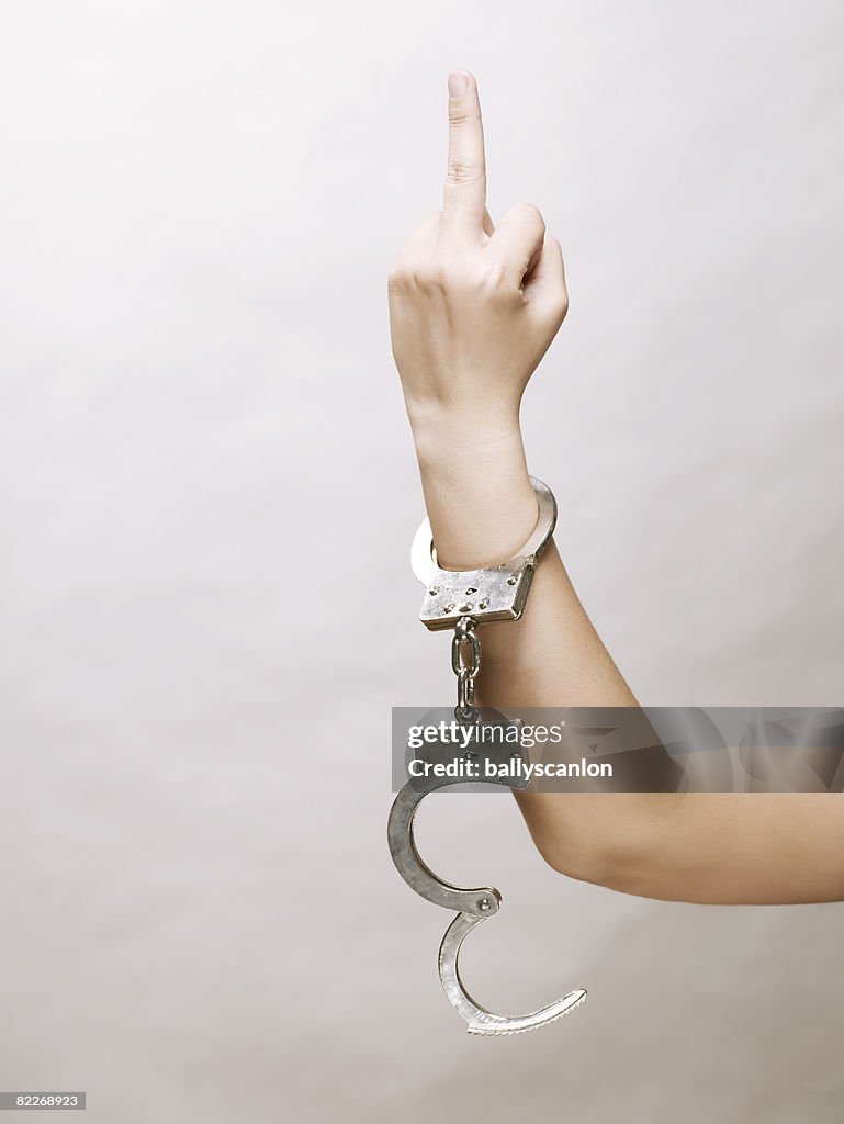 Young asian woman's arm, handcuffs, middle finger