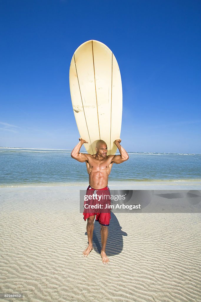 Man carries surfboard.