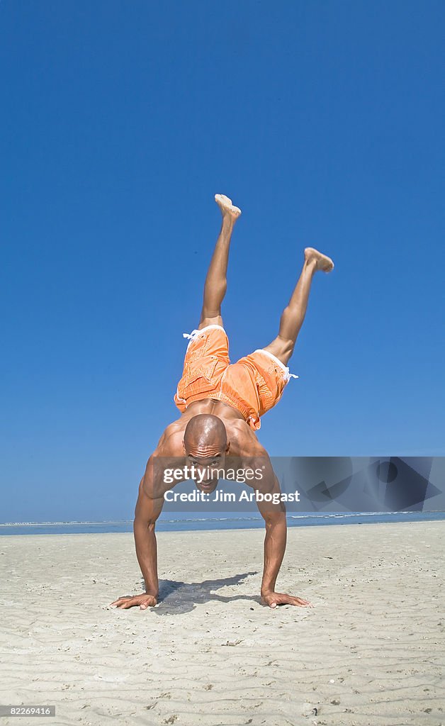 Man does a handstand on beach.